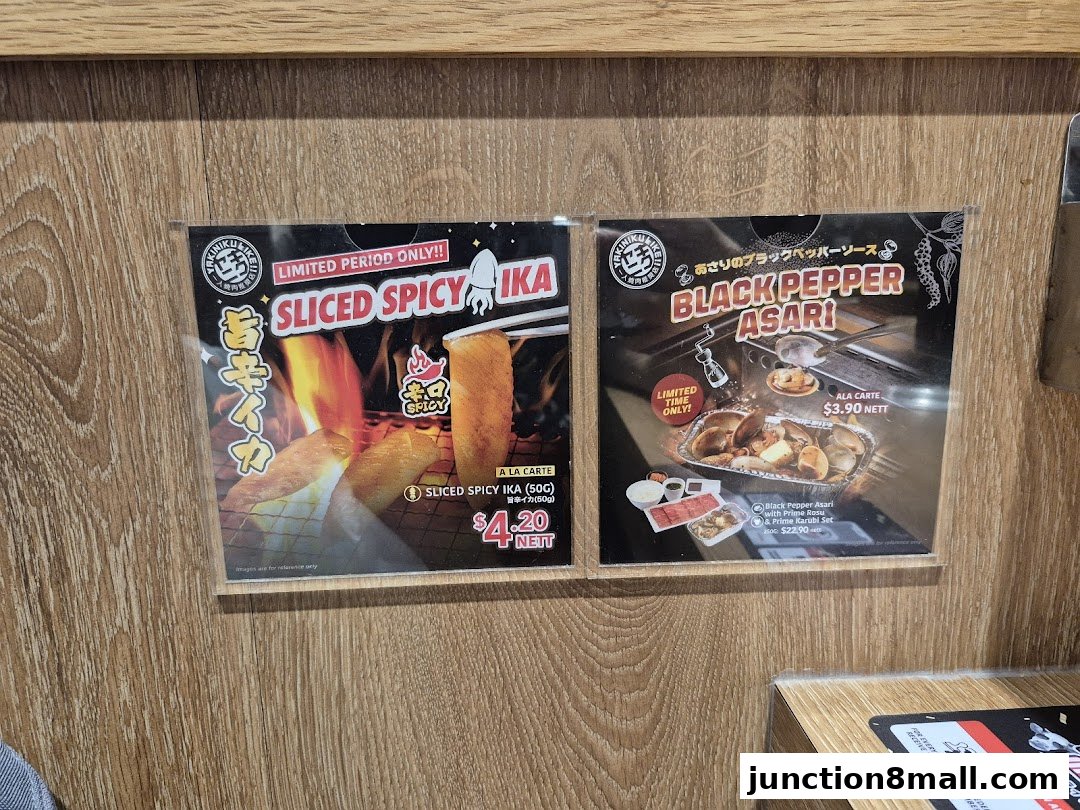 Two promotional signs for Yakiniku Like Junction 8, featuring limited-time spicy squid and black pepper clams.