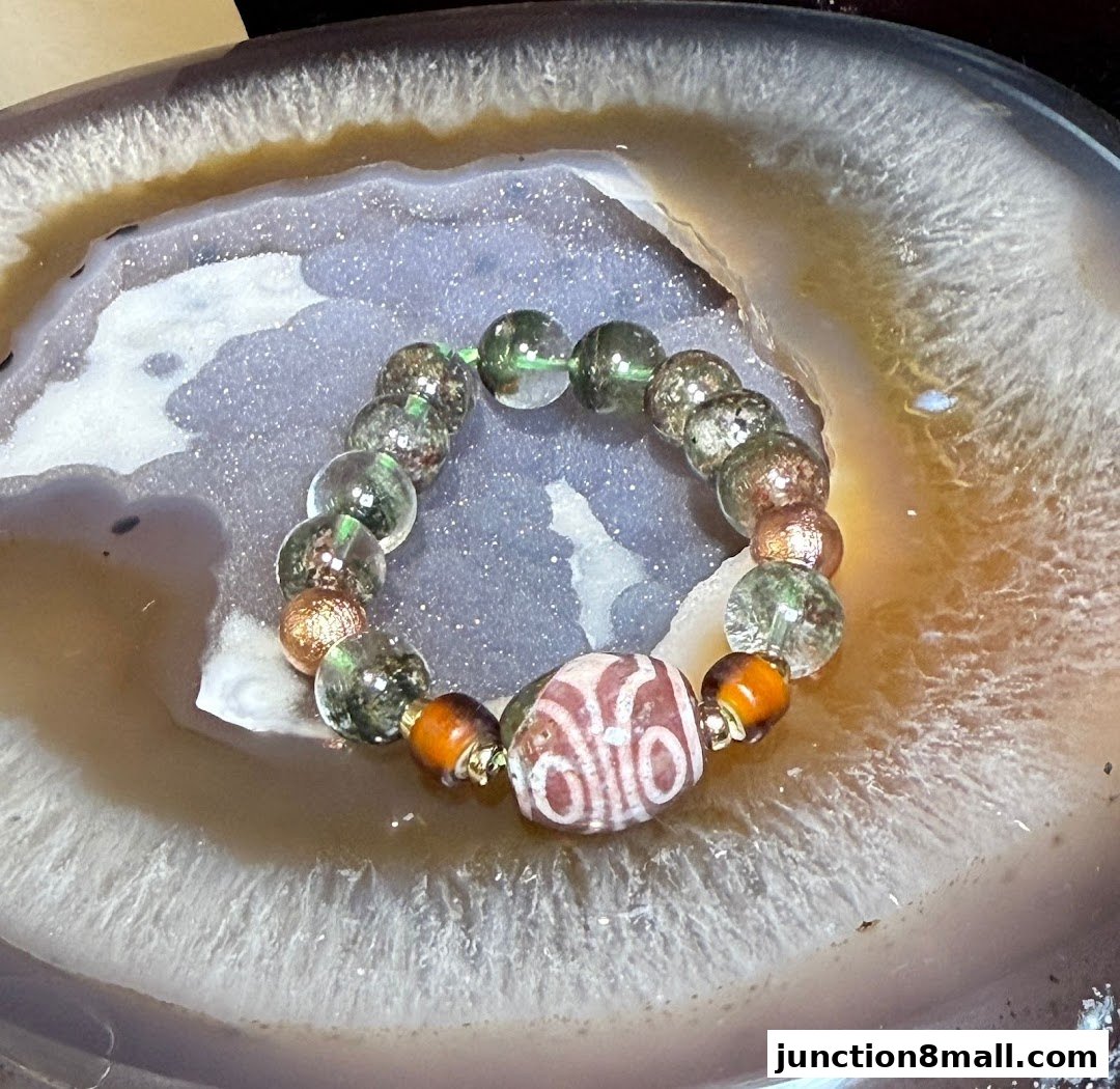 A close-up of a unique bracelet with green, clear, and copper beads, and a central patterned bead.