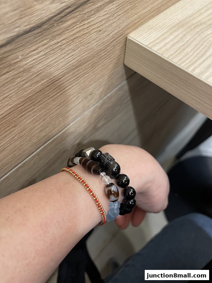A person's arm adorned with several beaded bracelets, including a red string bracelet and a black beaded bracelet with charms.