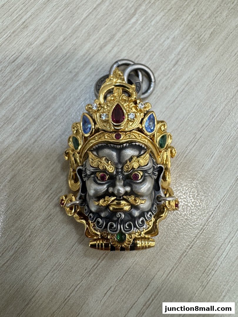 A detailed pendant featuring a fierce deity's face with gold and silver accents and colorful gemstones.