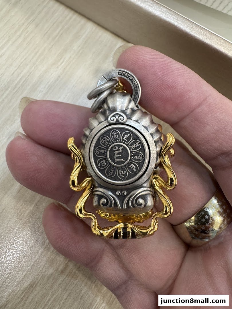 A hand holds a detailed silver and gold pendant with intricate carvings and symbols.