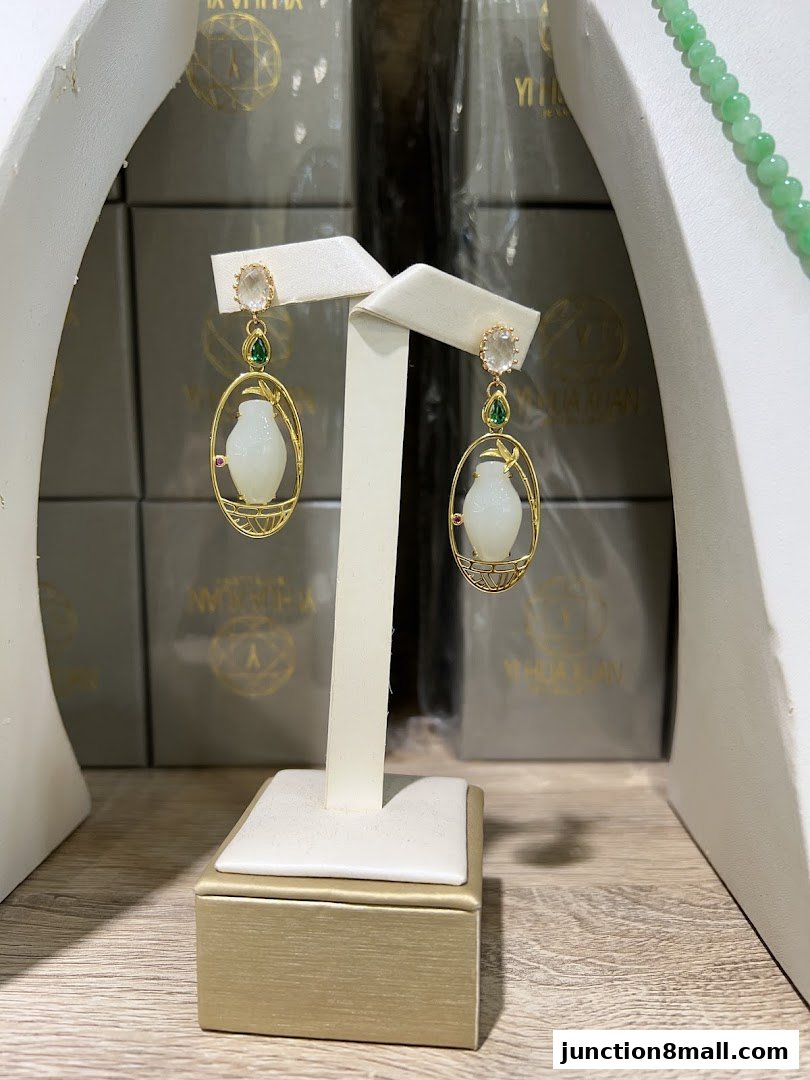 Elegant jade earrings with gold accents displayed on a stand, with branded boxes in the background.