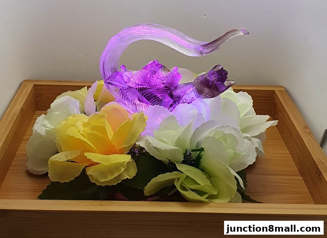 A decorative floral arrangement with artificial flowers and a glass sculpture illuminated by purple and white lights.