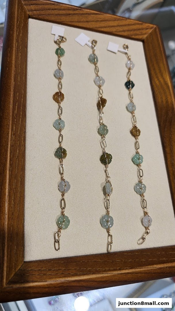 Three delicate bracelets with carved floral jade and gold chain links displayed.