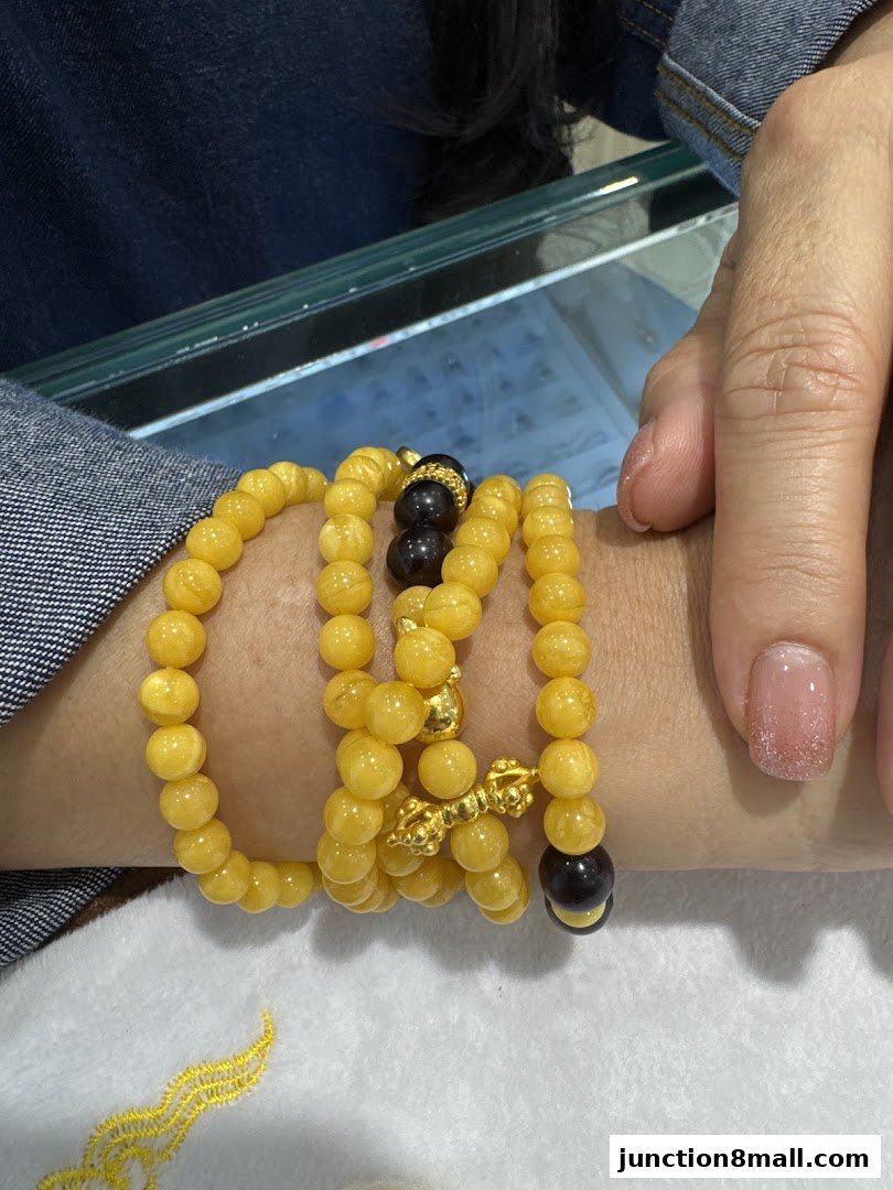 A person's arm wearing multiple yellow beaded bracelets with gold and dark stone accents.