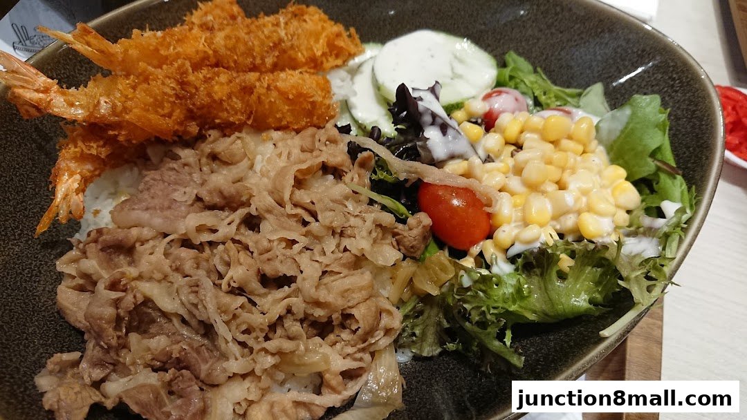 A delicious bowl of Yoshinoya's signature beef bowl with crispy shrimp and fresh salad.