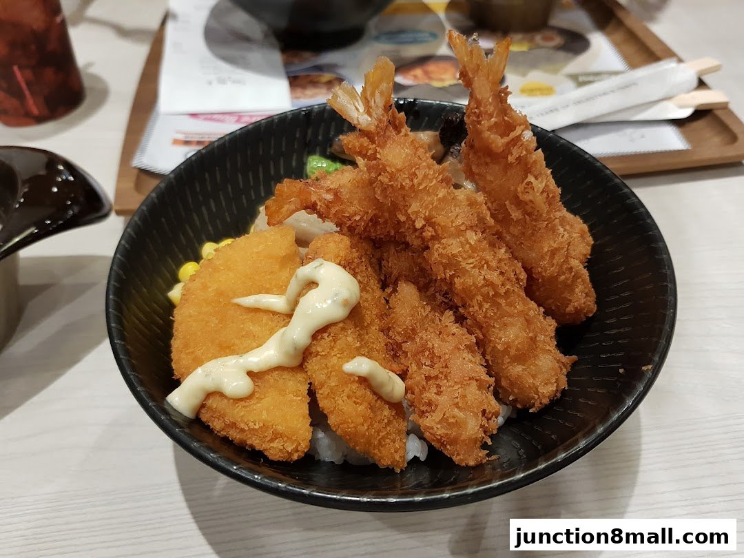 A bowl of rice topped with crispy fried shrimp and fish, drizzled with sauce.