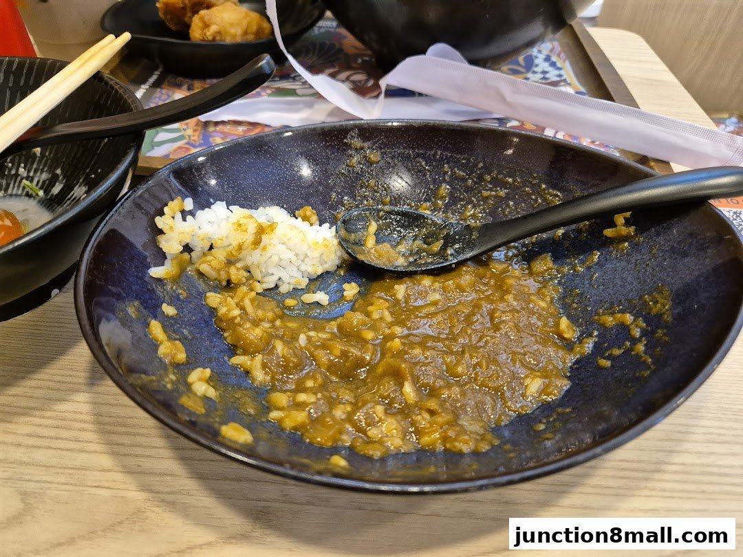 A close-up of a nearly finished bowl of Yoshinoya's signature curry rice with a spoon.