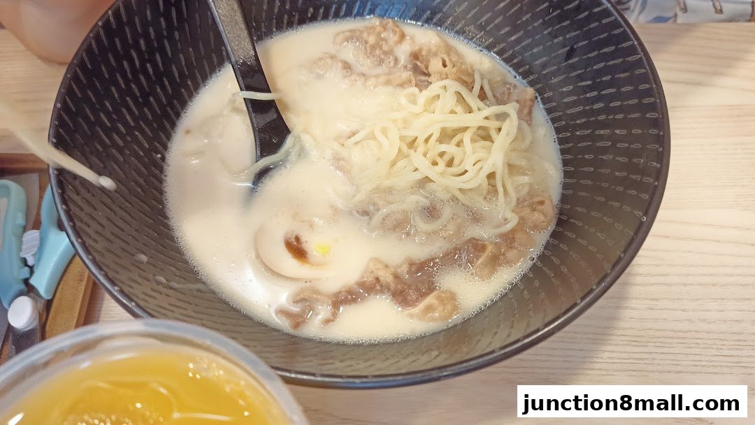 A close-up of a steaming bowl of ramen with noodles, meat, and egg in a creamy broth.