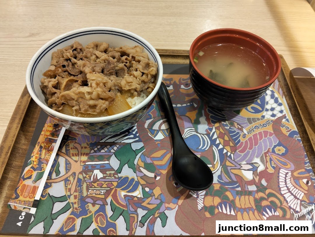 A Yoshinoya beef bowl meal with miso soup and a spoon on a colorful mat.