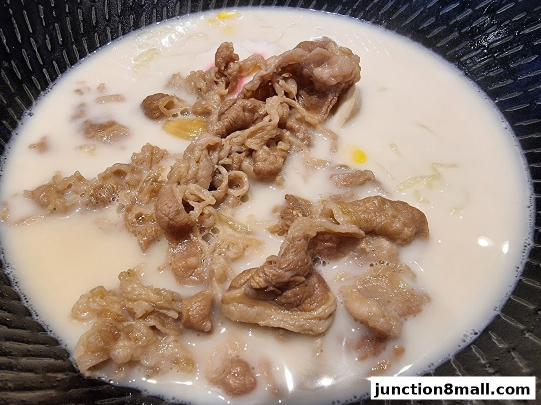 A close-up shot of a steaming bowl of beef noodle soup with thinly sliced beef.
