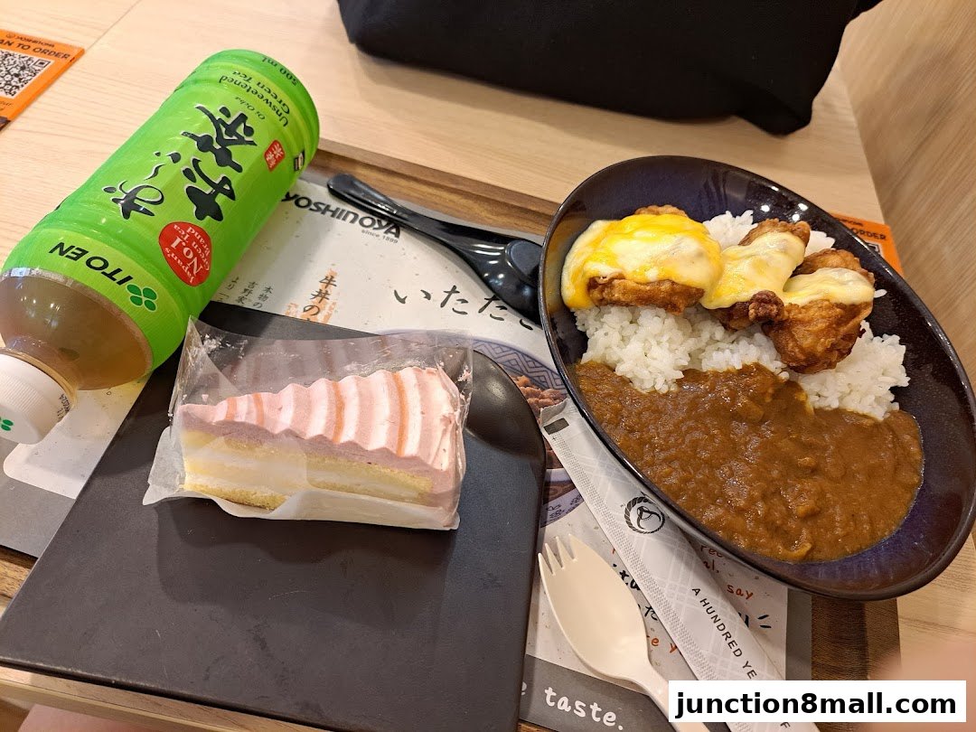A meal from Yoshinoya featuring curry rice with cheese-topped chicken, a slice of cake, and unsweetened green tea.