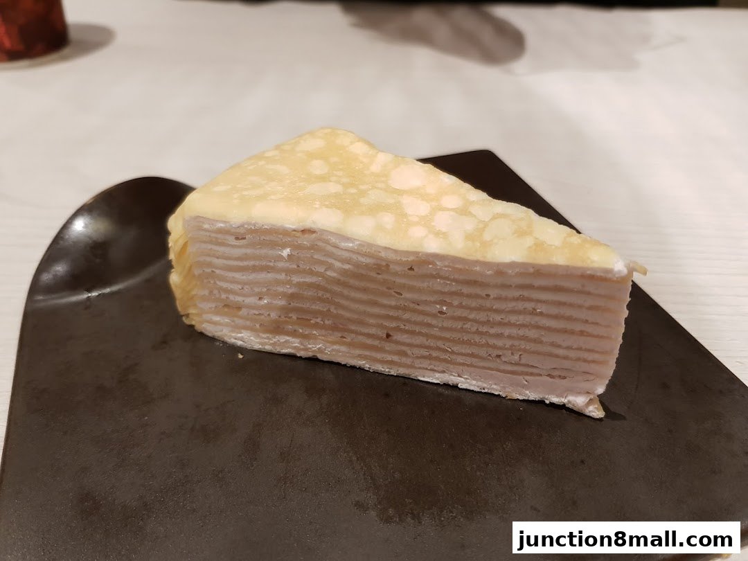 A slice of layered crepe cake with purple filling and a light yellow top layer.
